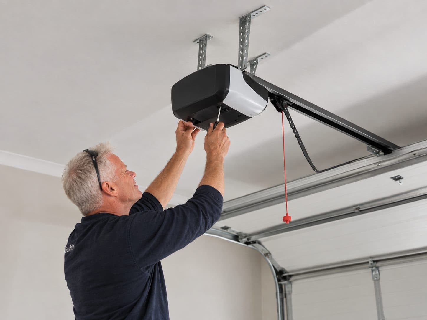 An installer reaching up to fit a garage door opener to the ceiling rail